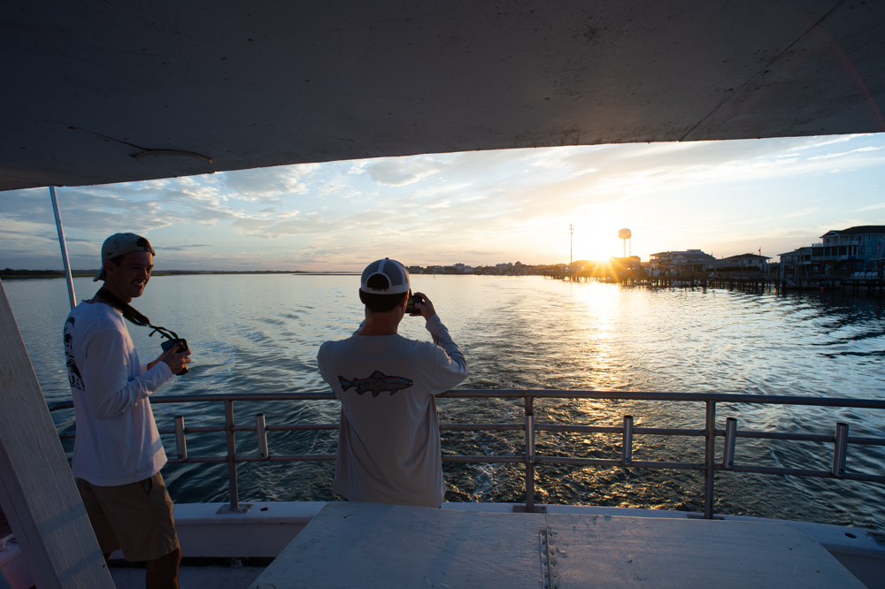 Brian's brother Kevin Davis, left, and his friend Ben Browndorf take pictures of the sunrise as the boat departs Topsail Beach through Banks Channel. (Port City Daily photo/Mark Darrough)