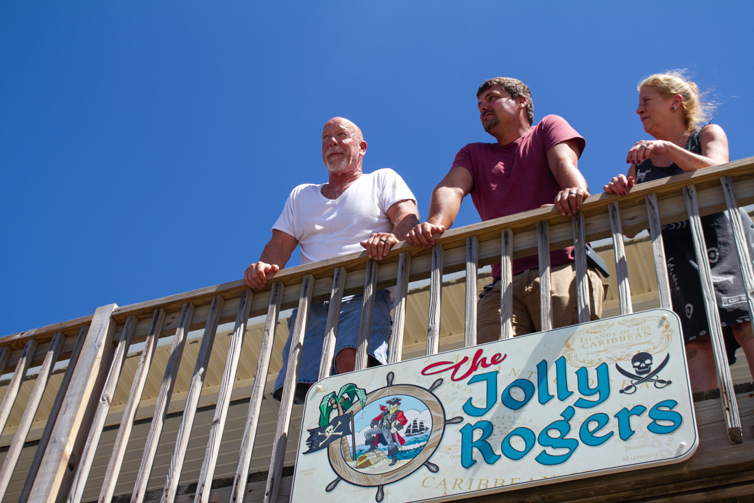 Mark Disher (left) and his wife Teri Disher (right) watch bulldozers move sand on East Beach Drive from the front porch of their rental. (Port City Daily photo/Johanna F. Still)
