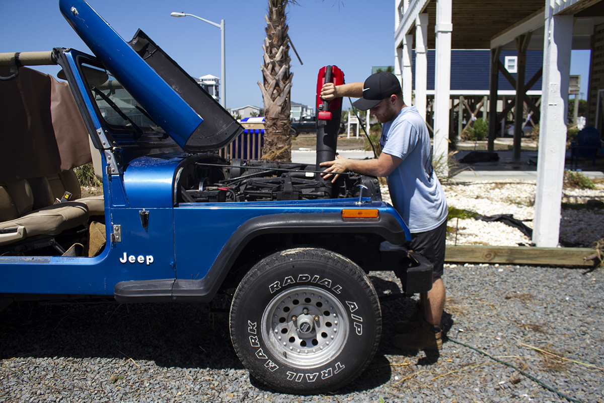 Trey Elmer uses a leaf blower to clear water out of a Jeep. After saltwater sputtered out of the exhaust pipe, the car ran. (Port City Daily photo/Johanna F. Still)